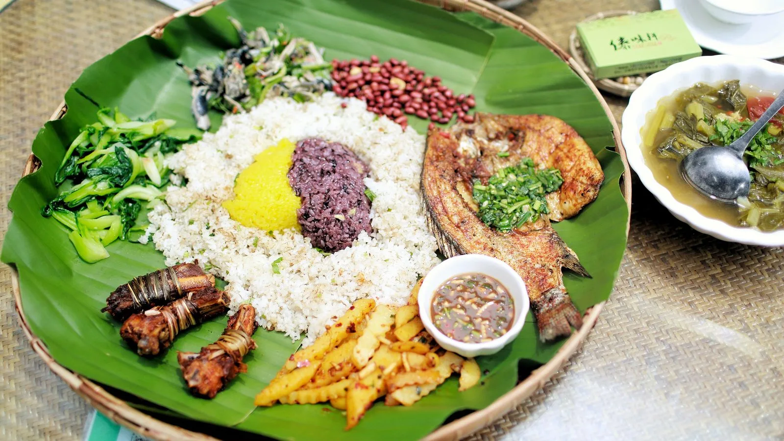 Delicious traditional Yunnan meal served on a banana leaf featuring rice, grilled fish, and vegetables.