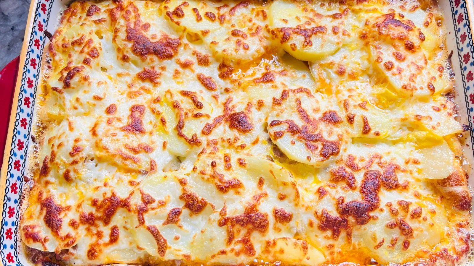 Delicious golden baked cheese and potato casserole in a decorative baking dish.