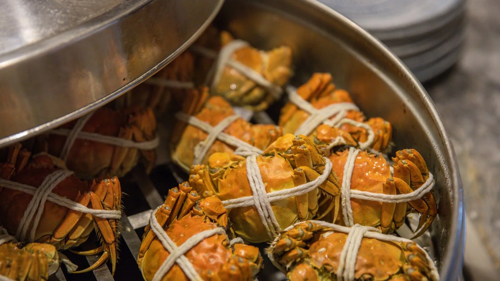 Close-up of tied crabs being steamed in a metal pot, ready for cooking.