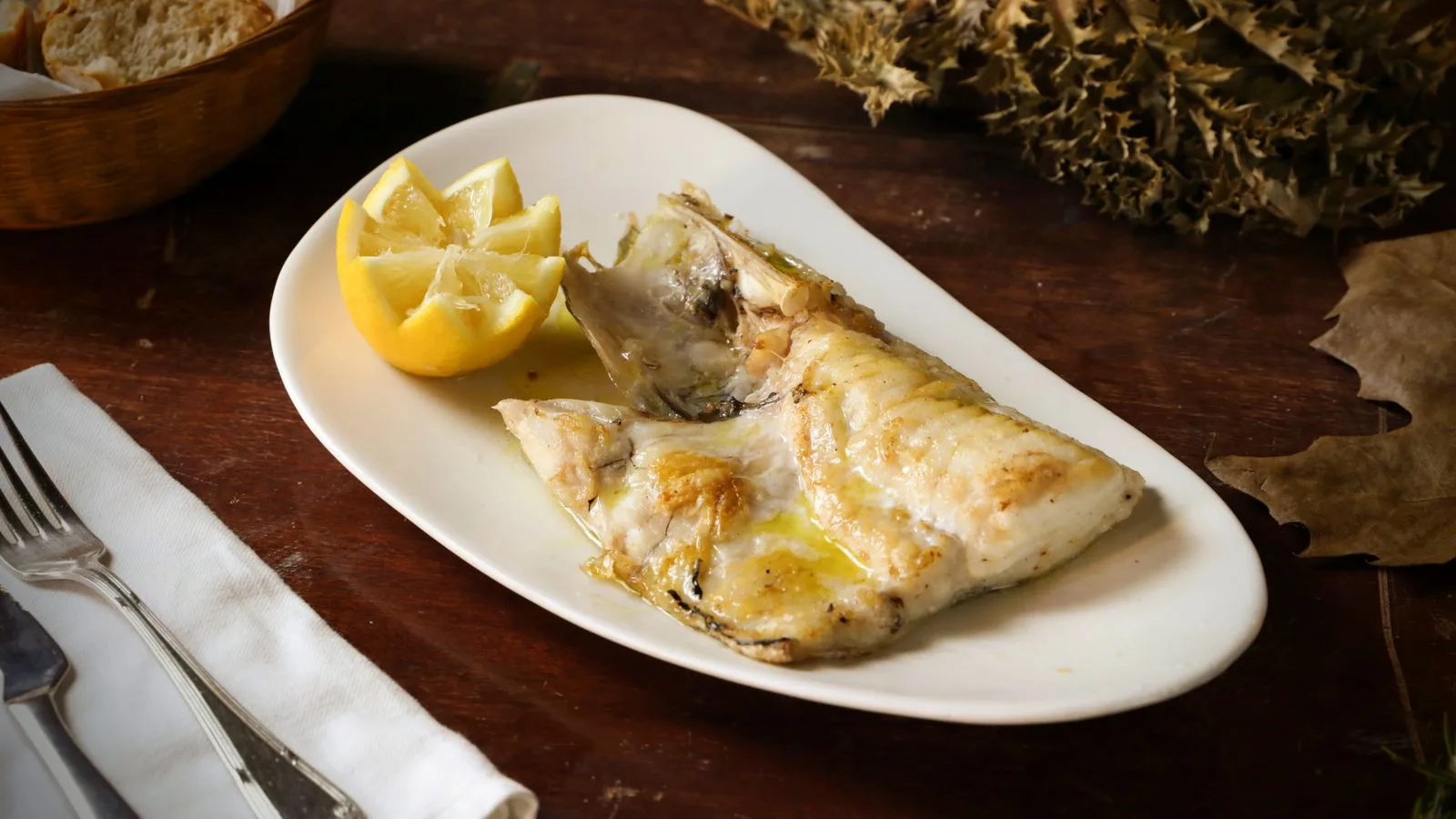 A plate of grilled fish served with lemon, bread, and a rustic autumn setting.