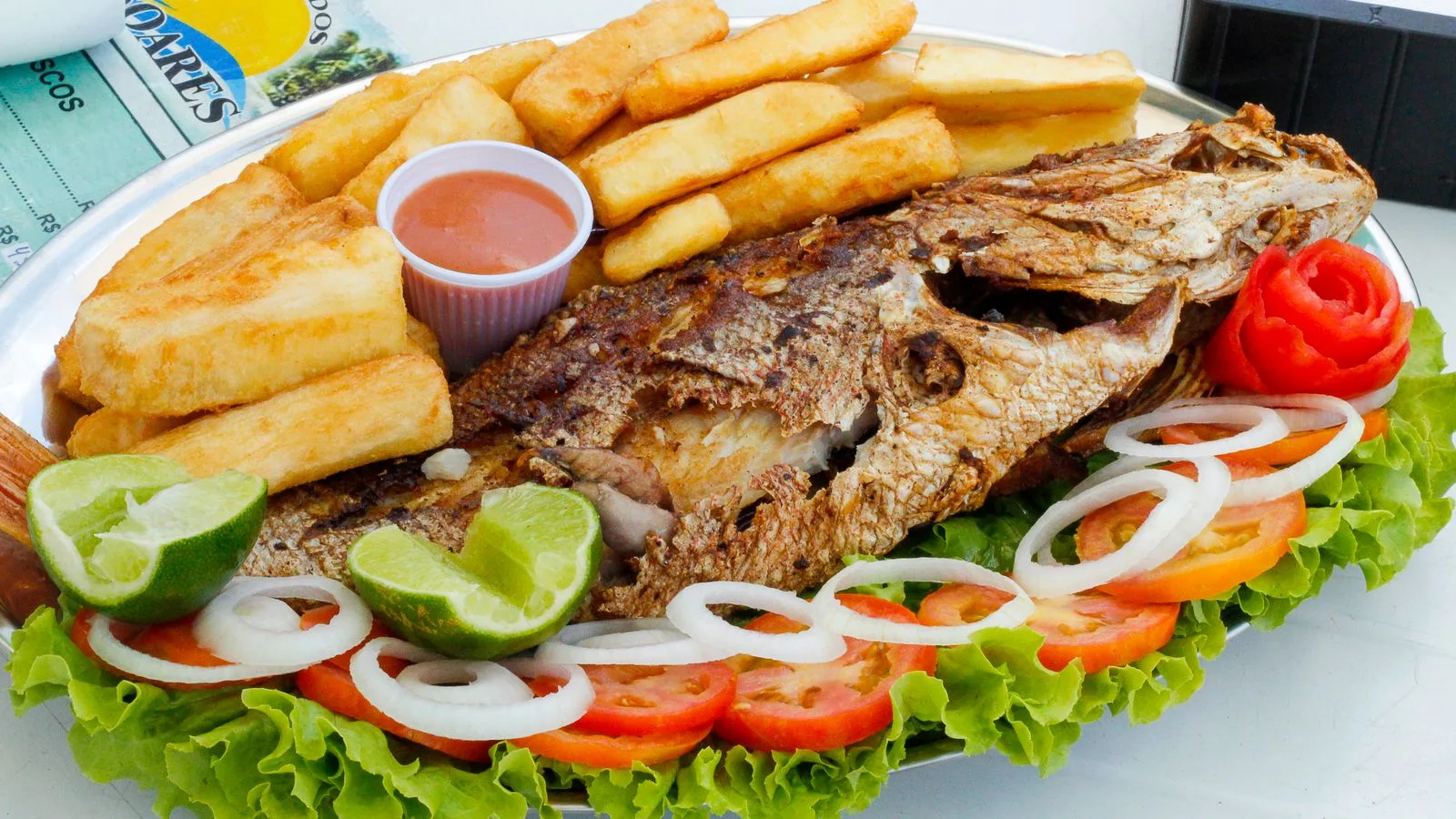 Mouth-watering grilled fish with fries, garnished with fresh vegetables, perfect for a Brazilian meal.