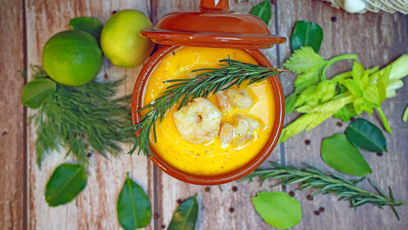 Top view of gourmet shrimp soup with rosemary and leafy greens.