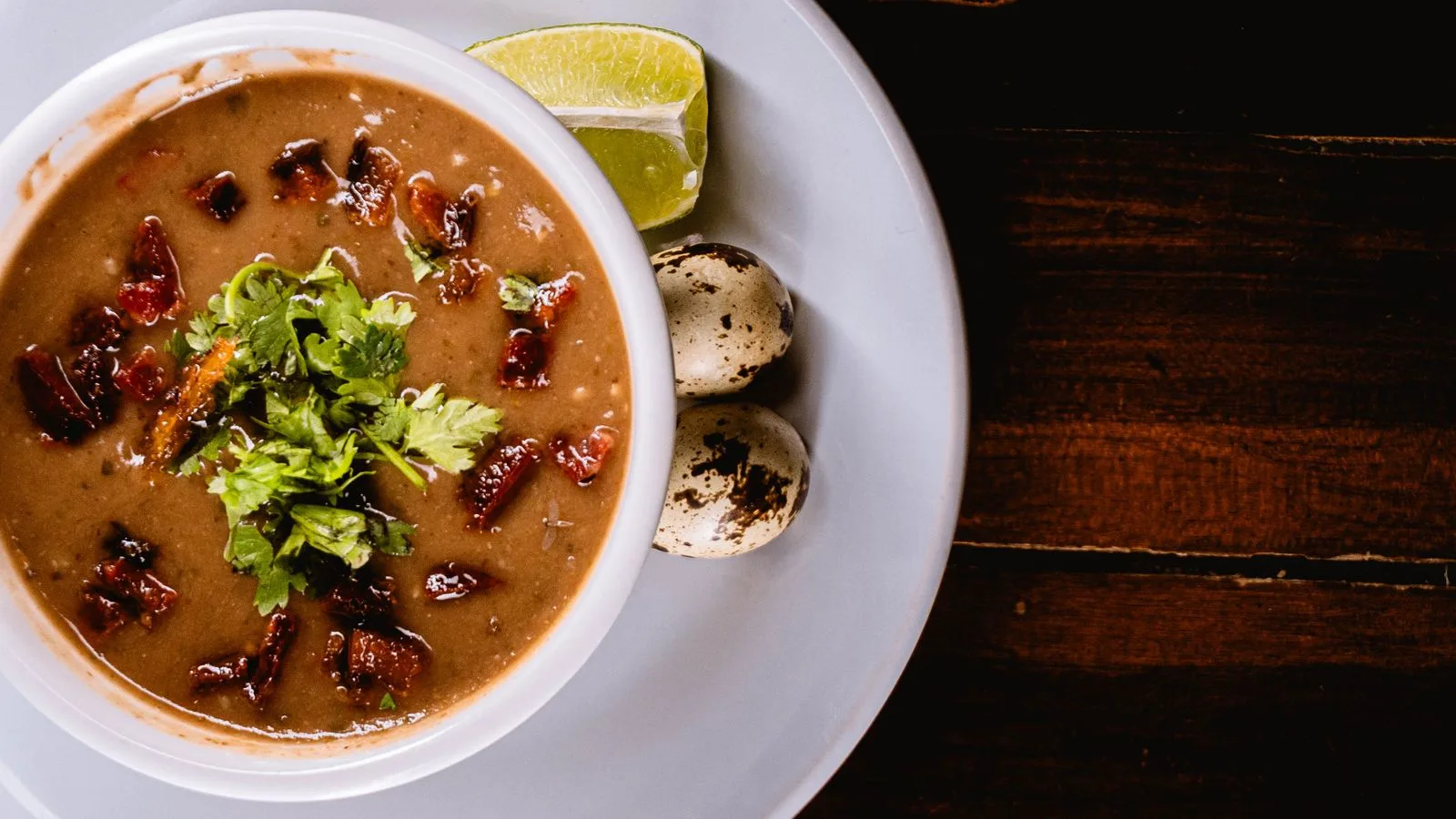 A savory bean soup garnished with herbs, quail eggs, and lime, perfect for a hearty meal.