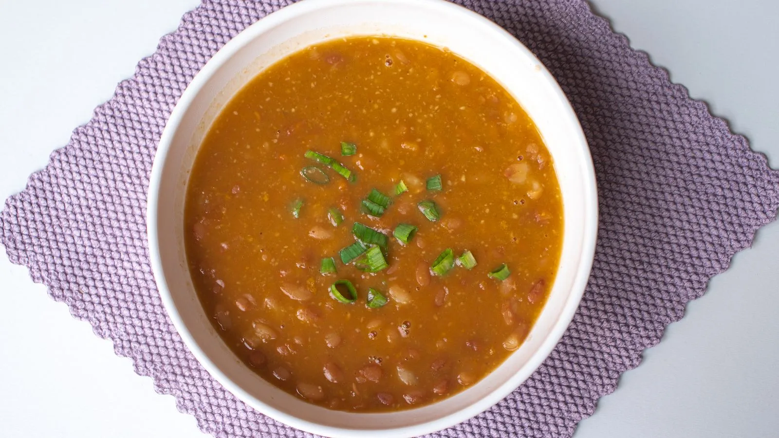 Hearty homemade bean soup garnished with green onions served in a white bowl.