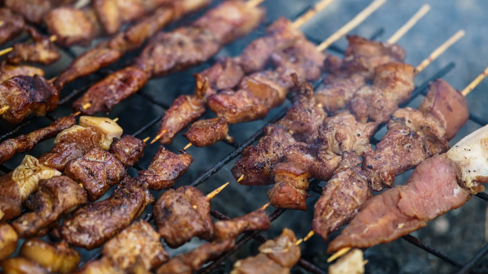 Delicious assortment of grilled meat skewers sizzling on an outdoor barbecue grill.