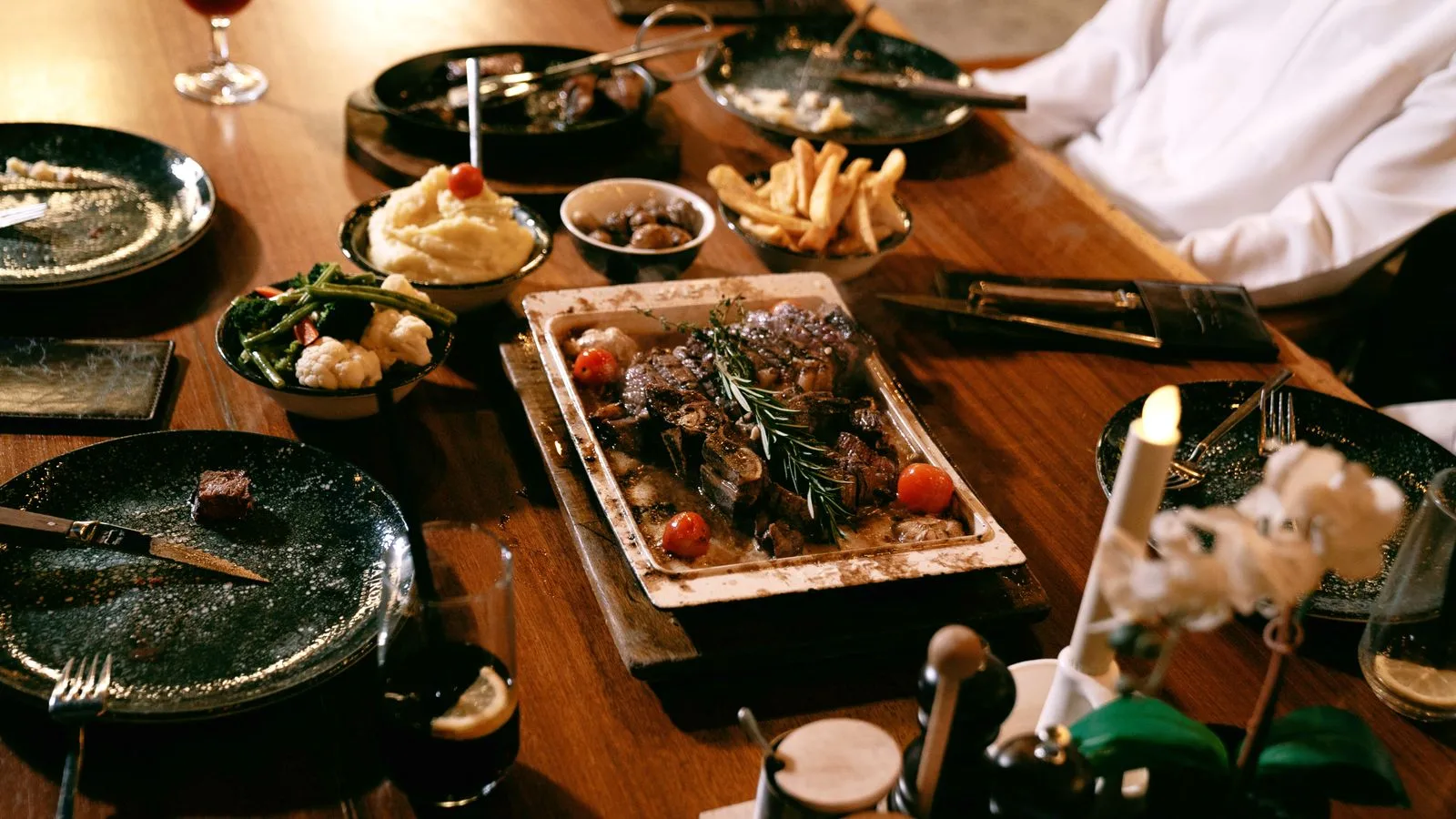 A cozy dinner table with grilled steak, sides, and wine creating a warm ambiance.