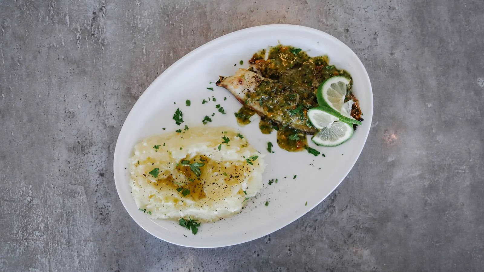 Top view of a meal featuring grilled fish with green sauce and mashed potatoes on a white plate.